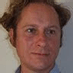 Close-up portrait of a man with light brown hair looking at the camera.