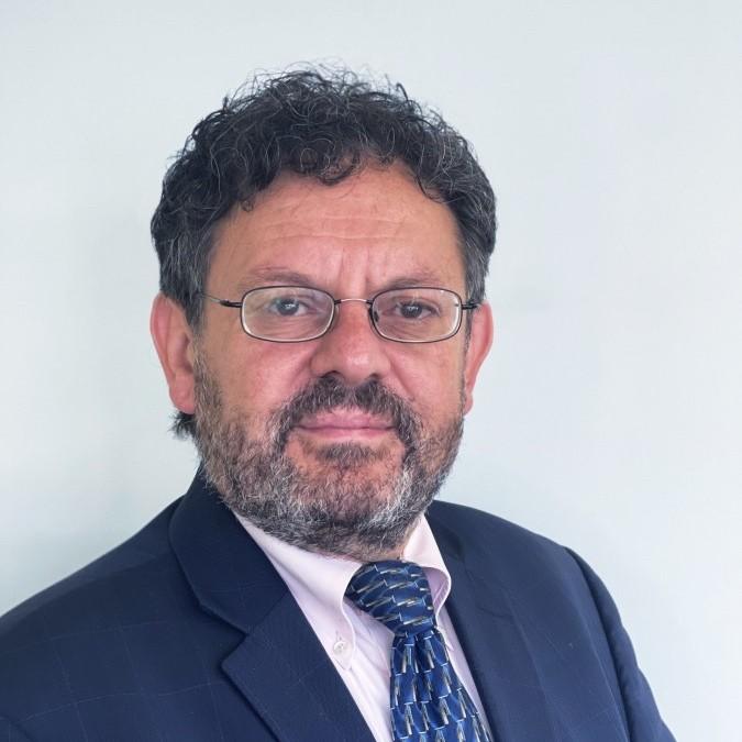 Professional headshot of a middle-aged man with dark hair and glasses, wearing a navy suit and blue patterned tie.
